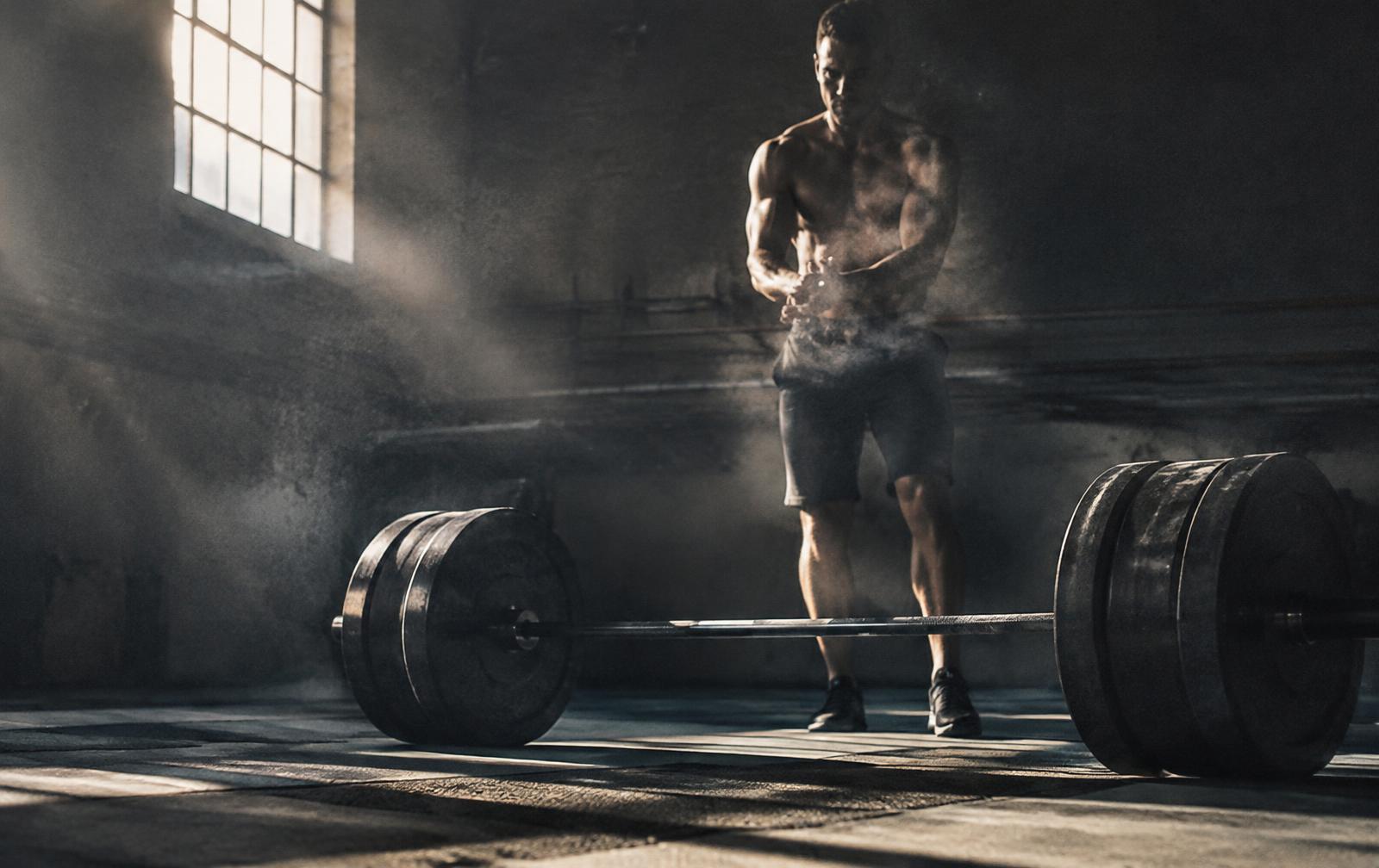 Athlete chalking up beside a loaded barbell in a raw industrial gym